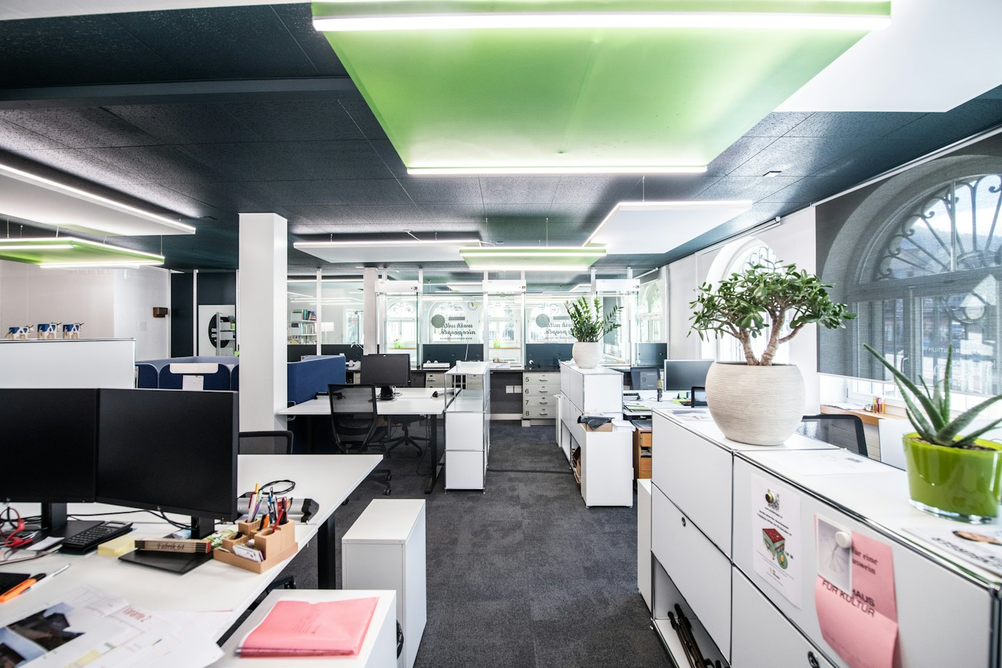 Kantor open-plan modern dengan meja kerja putih dan jendela besar.