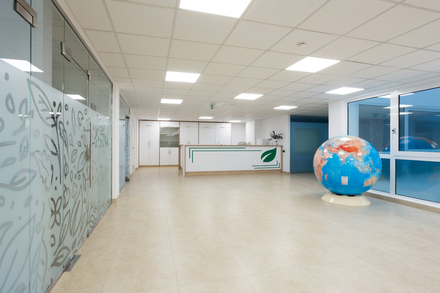Meja resepsionis kantor modern dengan bola dunia dan partisi kaca buram.